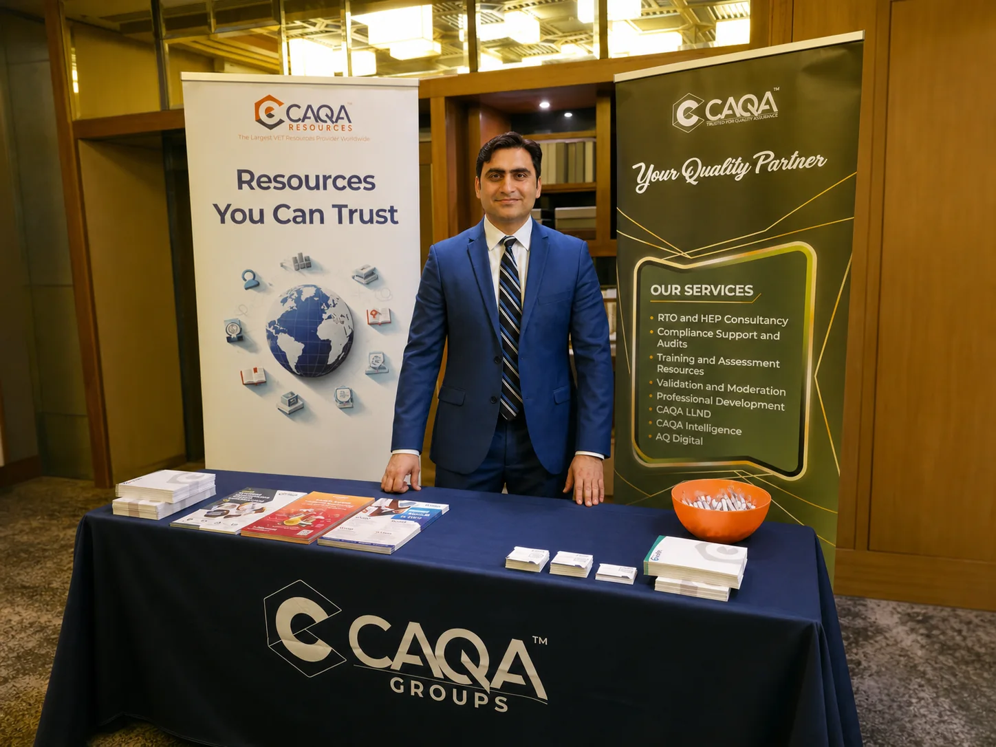 Sukh Sandhu stands at a trade show booth for CAQA Resources, discussing quality assurance services.