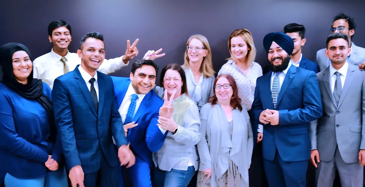 A diverse group of professionals pose for a cheerful team photo showcasing Sukh Sandhu's collaborative approach.