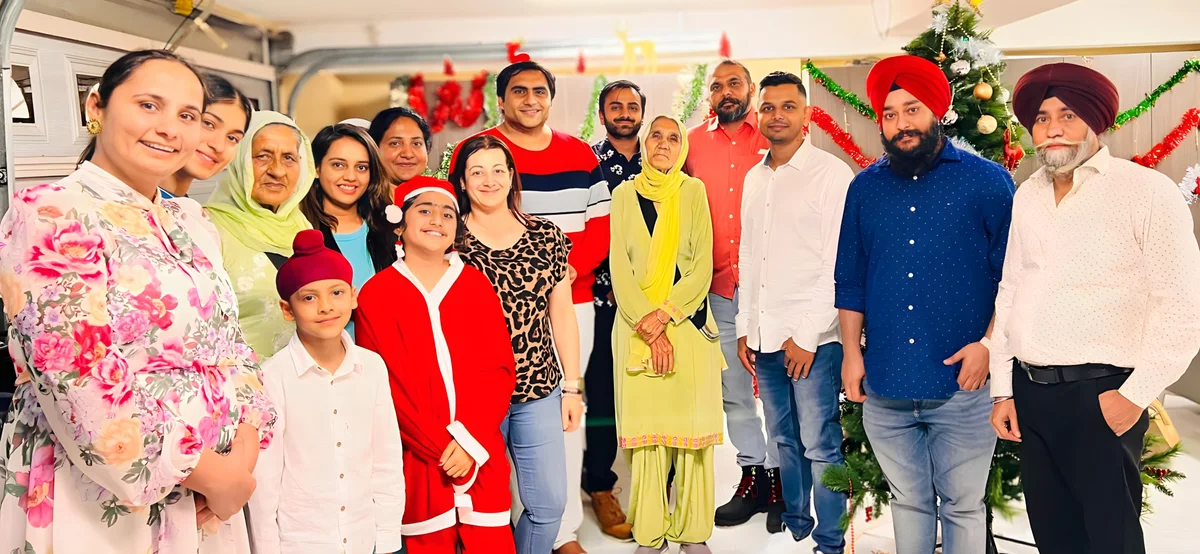 A large group including Sukh Sandhu poses for a holiday celebration with festive decorations.