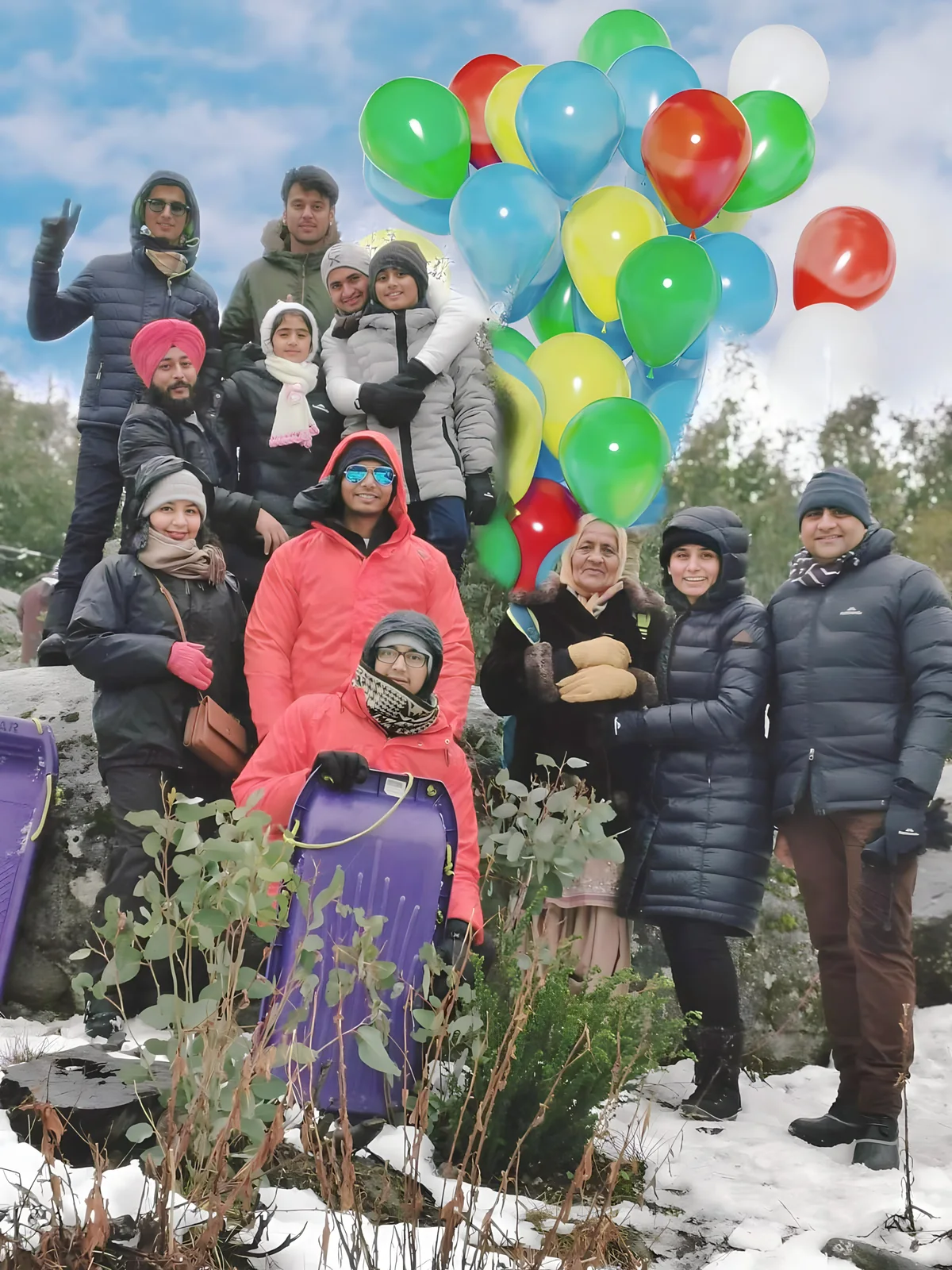 A large group poses with balloons and luggage in a snowy landscape during professional development.