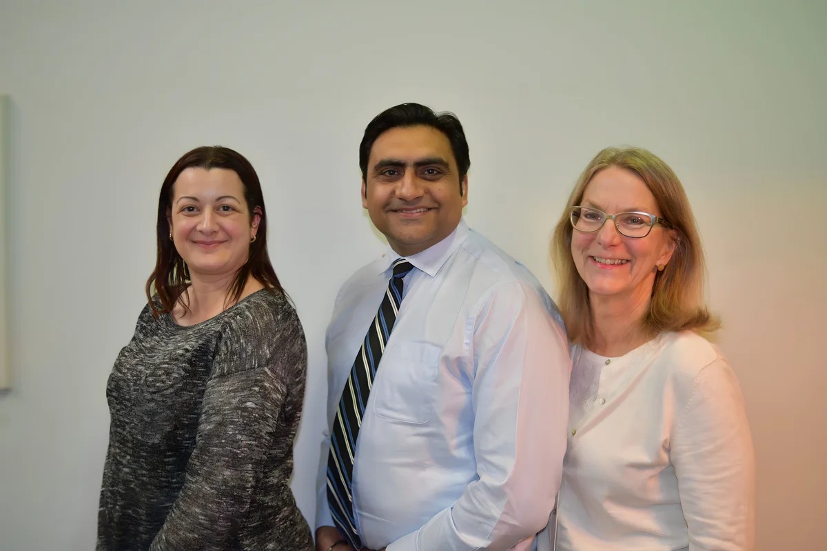 Sukh Sandhu poses with colleagues for a professional headshot, demonstrating quality assurance leadership.