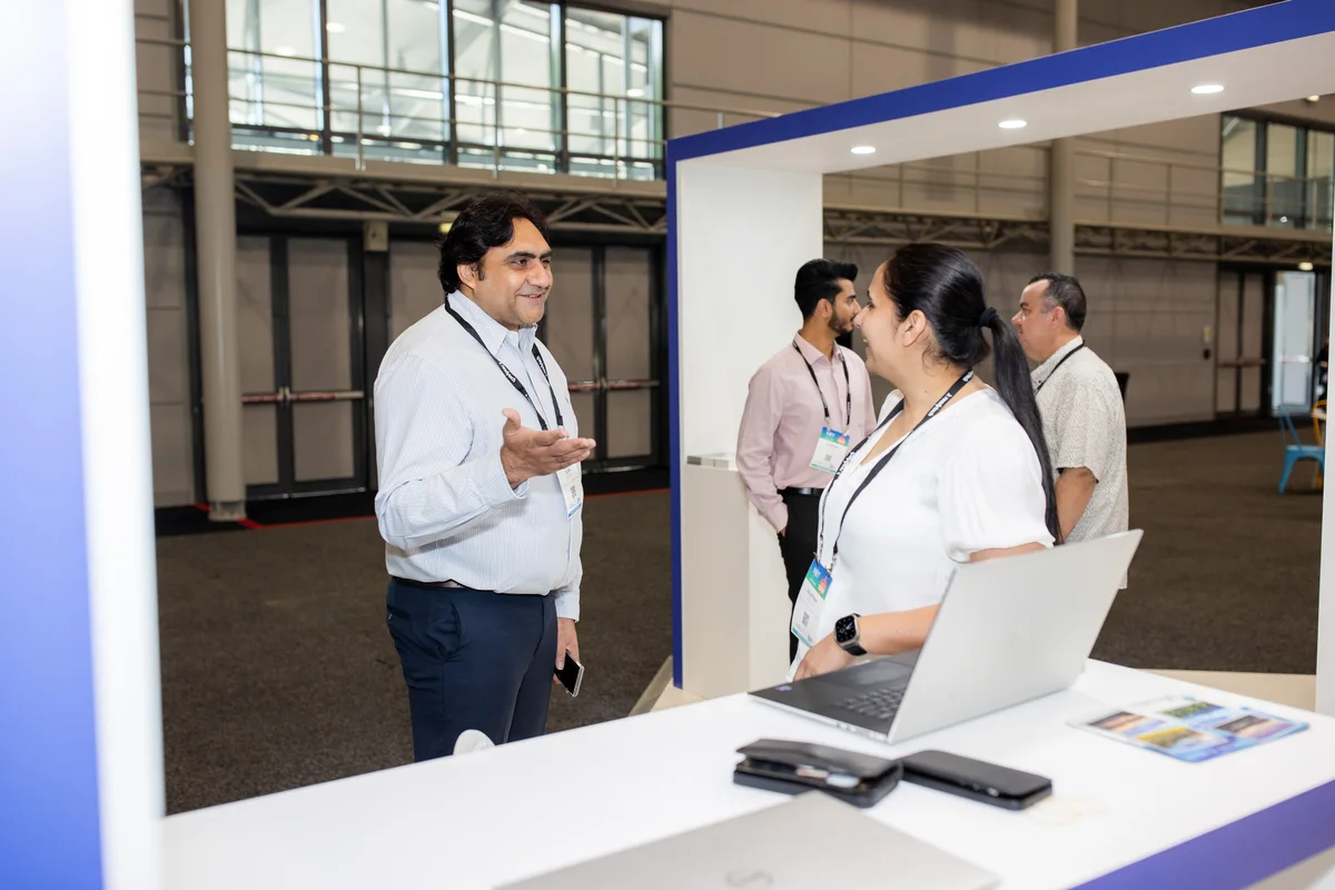 People discuss compliance solutions at a trade show with a laptop.