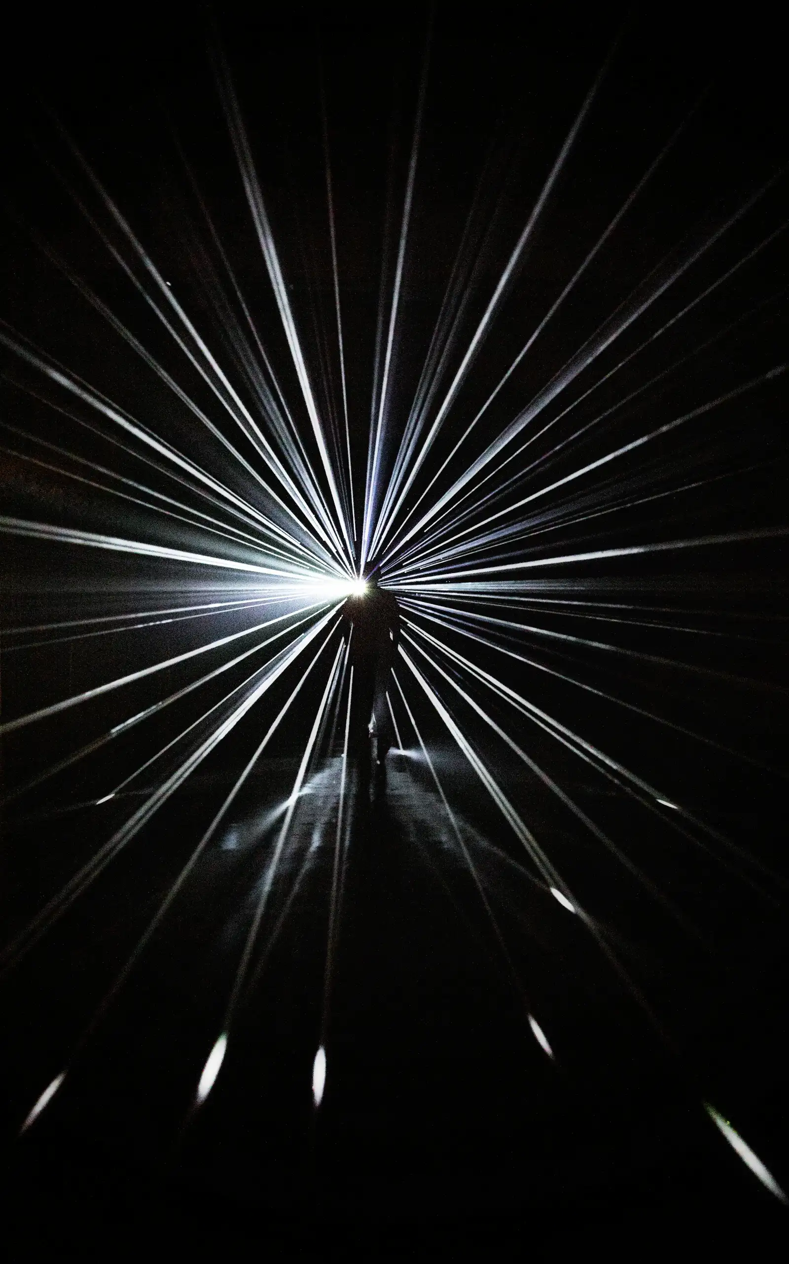A person stands amidst a radiating installation of bright white light beams, representing innovative compliance solutions.
