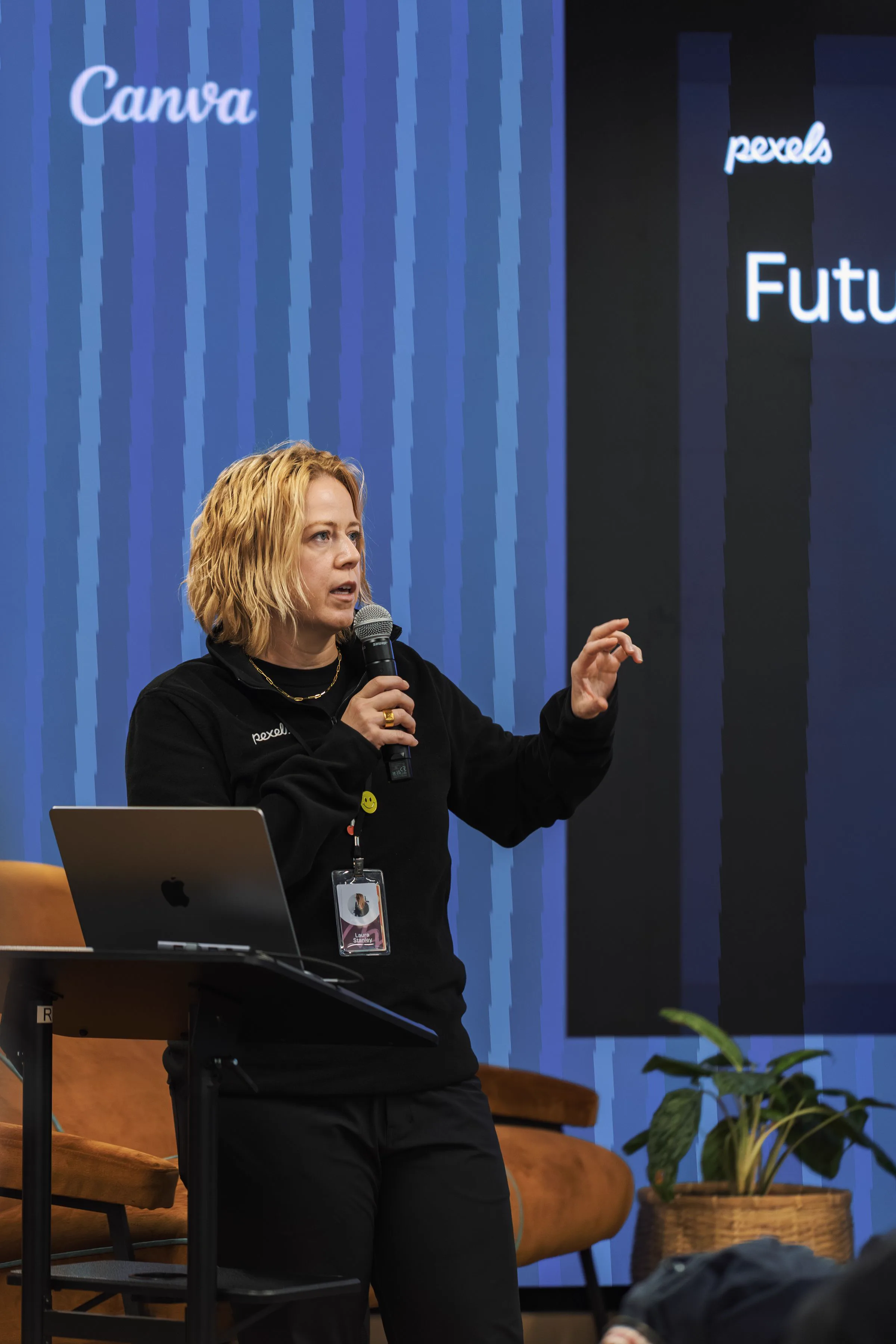 Conference Speaker | Sukh Sandhu A woman delivers a keynote presentation at a conference, with Canva and Pexels logos visible; compliance services are a key.